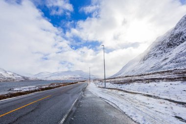 Norveç 'te sonbahar boyunca karlı dağlarla kaplı bir göl boyunca uzanan dolambaçlı bir yolun manzarası..