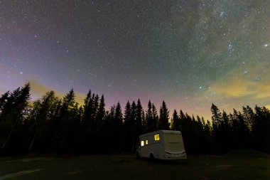 A motorhome parked under a starry sky with the northern lights visible in the forests of South Norway. clipart