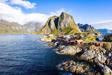 Norveç 'in Hamnoy, Lofoten Adaları' nda gün doğumu, kıyı şeridi boyunca geleneksel kırmızı evler ve dramatik dağlar..