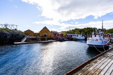 Norveç, Lofoten Adaları 'ndaki Nusfjord manzaralı, kırmızı ve sarı ahşap evler, tekneler ve kristal berrak sularla.