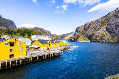 Norveç, Lofoten Adaları 'ndaki Nusfjord manzaralı, kırmızı ve sarı ahşap evler, tekneler ve kristal berrak sularla.
