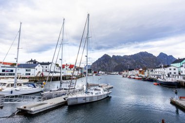 Norveç, Lofoten Adaları 'ndaki Henningsvaer manzarası liman boyunca uzanan ve arka planda dağlar bulunan geleneksel binaları gösteriyor..