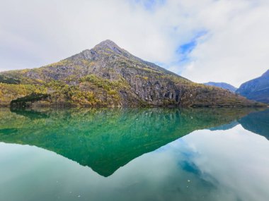 Autumn landscape in Skjolden, Norway, with a calm lake reflecting the mountains and colorful foliage. clipart