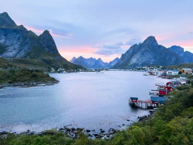Norveç 'in kuzeyindeki Reine, Lofoten Adaları' nda sonbahar günbatımı, dramatik dağlar, sakin sular ve kıyı boyunca geleneksel evler..