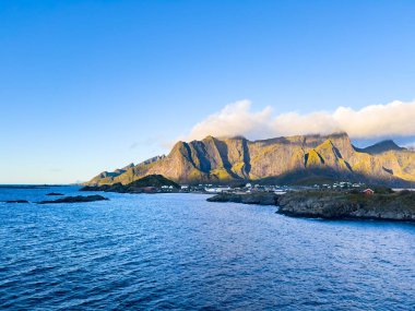 Norveç 'in Hamnoy, Lofoten Adaları' nda gün doğumu, kıyı şeridi boyunca geleneksel kırmızı evler ve dramatik dağlar..