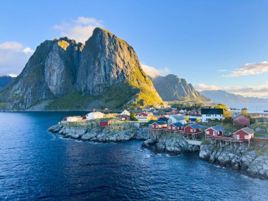 Norveç 'in Hamnoy, Lofoten Adaları' nda gün doğumu, kıyı şeridi boyunca geleneksel kırmızı evler ve dramatik dağlar..