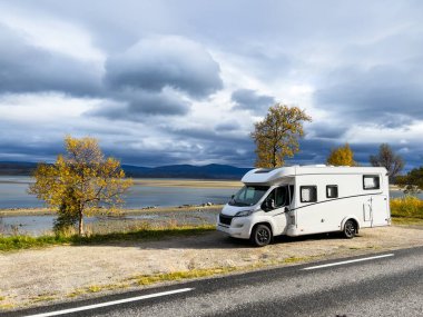 Sonbaharda göl kenarında karavan: bulutlu gökyüzü ve canlı renklerle sakin bir sahne