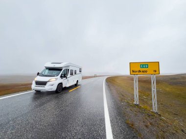 White camper van driving on e69 road to nordkapp, norway, in a rainy and foggy day clipart