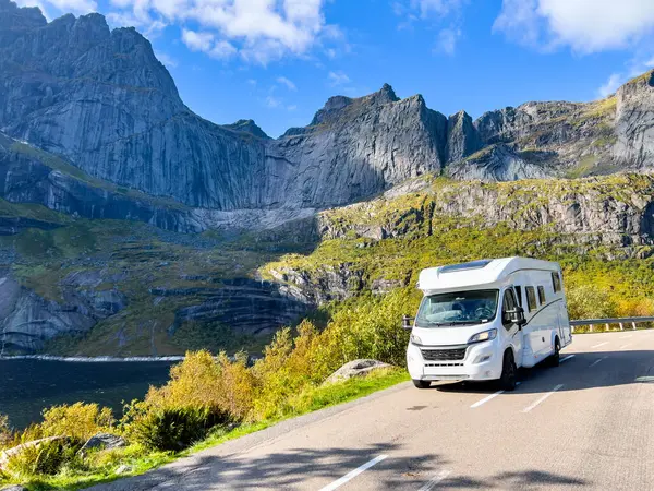 Norveç 'te dağların ortasındaki manzaralı bir yolda giden beyaz bir karavan seyahat ve macera manzarası sunuyor.