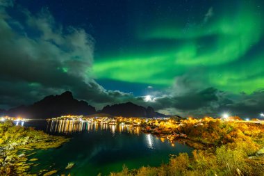 Kuzey Işıkları Reine üzerinde, Lofoten Adaları, Kuzey Norveç, gökyüzünü şehrin üzerinde canlı renklerle aydınlatıyor..