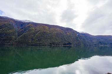 Norveç 'in Lustrafjorden kentindeki sonbahar manzarasında berrak su yansımaları, dağlar ve renkli yeşillikler yer almaktadır..
