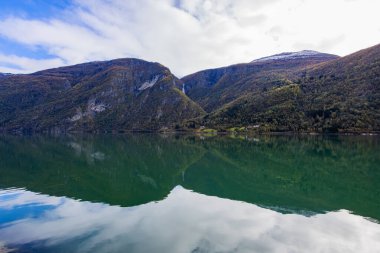 Norveç 'in Lustrafjorden kentindeki sonbahar manzarasında berrak su yansımaları, dağlar ve renkli yeşillikler yer almaktadır..