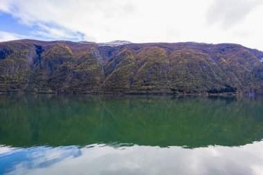Norveç 'in Lustrafjorden kentindeki sonbahar manzarasında berrak su yansımaları, dağlar ve renkli yeşillikler yer almaktadır..