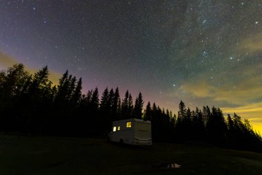 A motorhome parked under a starry sky with the northern lights visible in the forests of South Norway. clipart