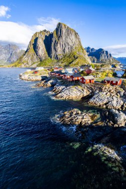 Norveç 'in Hamnoy, Lofoten Adaları' nda gün doğumu, kıyı şeridi boyunca geleneksel kırmızı evler ve dramatik dağlar..