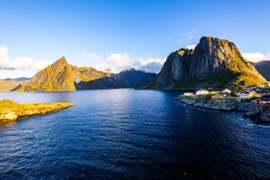 Norveç 'in Hamnoy, Lofoten Adaları' nda gün doğumu, kıyı şeridi boyunca geleneksel kırmızı evler ve dramatik dağlar..