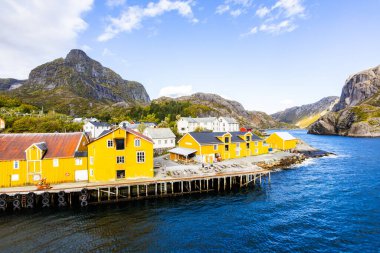 Norveç, Lofoten Adaları 'ndaki Nusfjord manzaralı, kırmızı ve sarı ahşap evler, tekneler ve kristal berrak sularla.