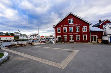 A scenic view of Henningsvaer in Lofoten Islands, Norway, showcasing traditional buildings along the harbor with mountains in the background. clipart