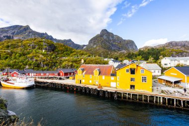 Norveç, Lofoten Adaları 'ndaki Nusfjord manzaralı, kırmızı ve sarı ahşap evler, tekneler ve kristal berrak sularla.