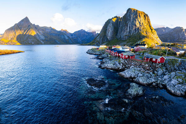Sunrise over Hamnoy, Lofoten Islands, Norway, with traditional red houses and dramatic mountains along the coastline.