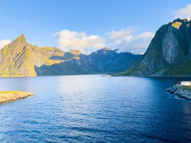 Norveç 'in Hamnoy, Lofoten Adaları' nda gün doğumu, kıyı şeridi boyunca geleneksel kırmızı evler ve dramatik dağlar..