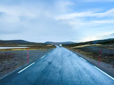Yağmurlu bir günde İskoç dağlarında ıslak bir yolda giden beyaz bir karavan.