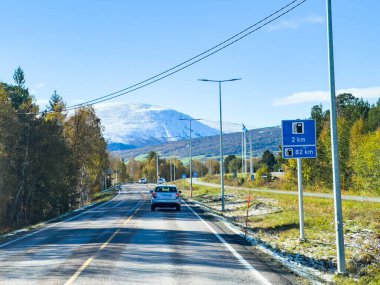 Güzel manzaralı bir güzergah, parlak sonbahar manzarası boyunca kar kaplı görkemli bir dağ zirvesine doğru ilerlerken berrak mavi gökyüzünün zeminine karşı.
