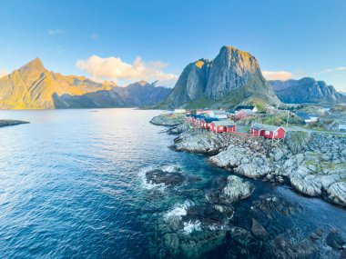 Norveç 'in Hamnoy, Lofoten Adaları' nda gün doğumu, kıyı şeridi boyunca geleneksel kırmızı evler ve dramatik dağlar..