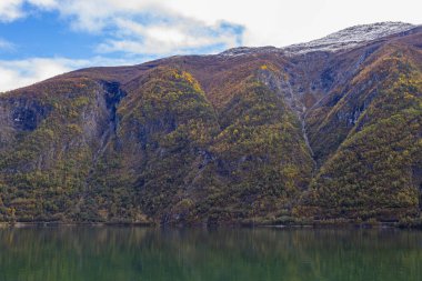 Autumn landscape in Lustrafjorden, Norway, featuring clear water reflections, mountains, and colorful foliage. clipart