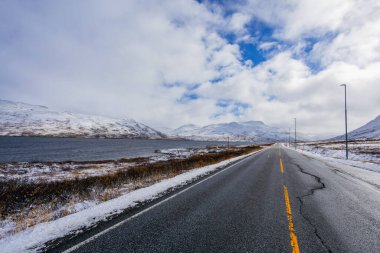 Norveç 'te sonbahar boyunca karlı dağlarla kaplı bir göl boyunca uzanan dolambaçlı bir yolun manzarası..