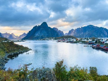 Autumn sunset in Reine, Lofoten Islands, northern Norway, with dramatic mountains, calm waters, and traditional houses along the shore. clipart