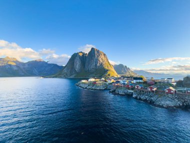 Sunrise over Hamnoy, Lofoten Islands, Norway, with traditional red houses and dramatic mountains along the coastline. clipart