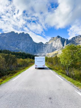 Norveç 'te dağların ortasındaki manzaralı bir yolda giden beyaz bir karavan seyahat ve macera manzarası sunuyor.