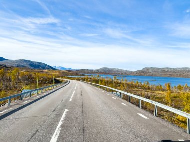 Motorhome driving on a scenic road in Kiruna, Sweden, with autumn foliage and beautiful lake. clipart