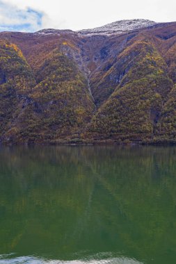 Norveç 'in Lustrafjorden kentindeki sonbahar manzarasında berrak su yansımaları, dağlar ve renkli yeşillikler yer almaktadır..