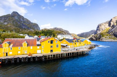 Norveç, Lofoten Adaları 'ndaki Nusfjord manzaralı, kırmızı ve sarı ahşap evler, tekneler ve kristal berrak sularla.