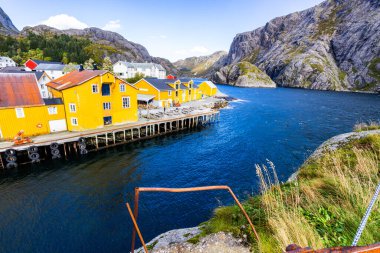 Norveç, Lofoten Adaları 'ndaki Nusfjord manzaralı, kırmızı ve sarı ahşap evler, tekneler ve kristal berrak sularla.