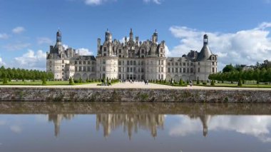 Chambord Şatosu, berrak mavi gökyüzüne karşı çarpıcı mimarisini sergileyerek çevredeki suları görkemli bir şekilde yansıtıyor.
