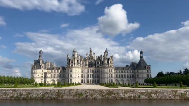 Fransız Rönesans mimarisinin çarpıcı bir örneği olan Chambord Şatosu, mavi gökyüzü ve yeşillik arkaplanının karşısında görkemli bir şekilde duruyor.