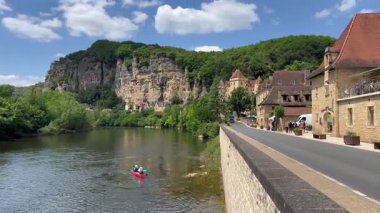 Dordogne, Fransa 'nın Dordogne kentindeki kayalıkların eteklerine kurulmuş güzel bir köy olan La Roque Gageac yakınlarındaki Dordogne nehrinde kürek çeken kayakçılar.