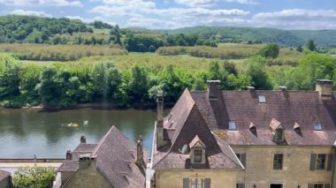 Fransa 'nın La Roque Gageac kentindeki gri kiremitli çatıları olan evlerin yakınındaki Dordogne nehrinde kanolar yüzüyor.
