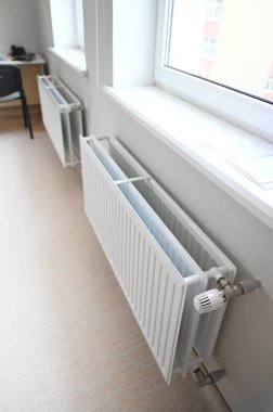 Odaya sıcaklık ve konfor sağlayan beyaz bir radyatör duvara tutturulmuş. Pürüzsüz yüzeyi ve nötr rengi etrafındaki dekora kusursuz bir şekilde karışır.