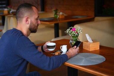 Sakallı adam sakin bir kafede oturur, kahvesini yudumlar ve yalnızlığın tadını çıkarır. Atmosfer sakin, sohbetin hafif uğultusu ve taze demlenmiş kahvenin kokusu havayı dolduruyor.