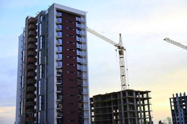 Şehir merkezinde inşaat halindeki yeni yüksek binalar. İşçiler şehir manzarasına yeni eklemeler yaparken, vinçler ve iskeleler ufuk çizgisine karşı görülebilir..