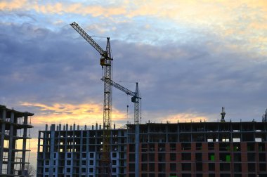 Şehir merkezinde inşaat halindeki yeni yüksek binalar. İşçiler şehir manzarasına yeni eklemeler yaparken, vinçler ve iskeleler ufuk çizgisine karşı görülebilir..