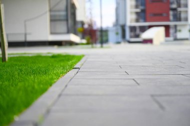 Uzun, modern şehir evlerinin önünde yeşil bir çimen uzanır, hareketli şehir manzarasına sakin bir kontrast sunar..