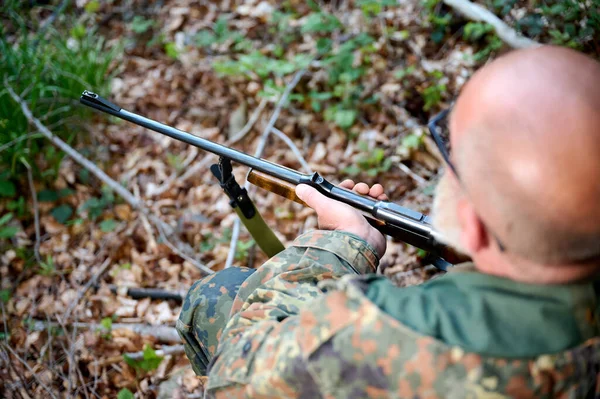 灰胡子的老猎手手里拿着来福枪 在打猎时瞄准 坐在森林的木制原木上观察大自然 狩猎和旅行的概念 — 图库照片