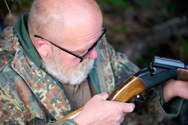 Avcının tüfeğe bakarken çekilmiş görüntüsü. Hunter silahı kontrol ediyor. Kamuflaj elbisesi ve gözlüklü adamın yakın görüntüsü ateş ettikten sonra silahın durumunu kontrol ediyor..