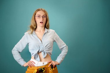 Arka planda alet kemeri olan şaşırmış genç kadın işçinin portresi. Yeni bir proje planlayan beyaz bir kadın. Stüdyoda portre. Boşluğu kopyala.