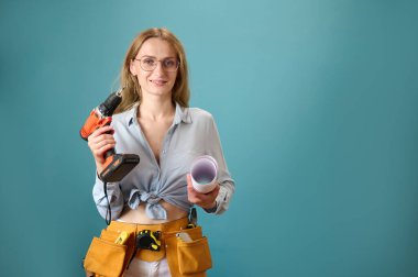 Koruyucu kasklı genç bir kadın işçi arka planda izole edilmiş bir ev planı tutuyor. Güzel gülümseyen beyaz kadın mimar yeni bir proje planlıyor. İnsanlar mimarlık projesinde çalışıyor